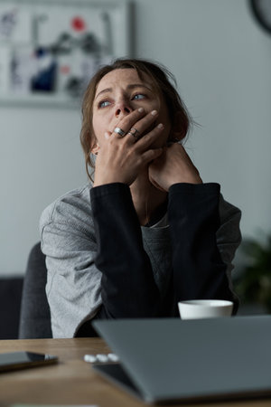A young woman sits in her home looking contemplative and troubled, lost in her thoughts.のeditorial素材