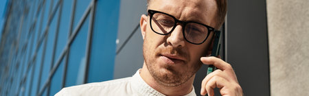 A young man teaching at a university talks on the phone outside a contemporary building.