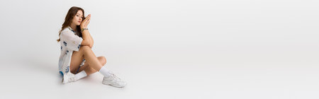 A young woman poses confidently in stylish attire within a minimalist setting.