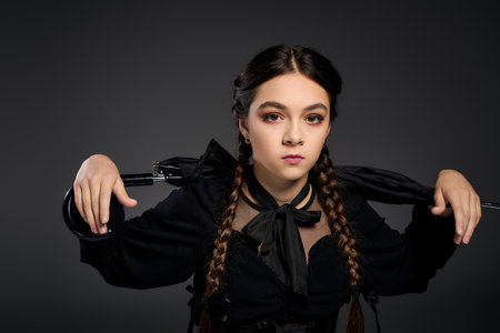 A girl with braids wears a Wednesday costume inspired by Halloween, expressing spooky charm.