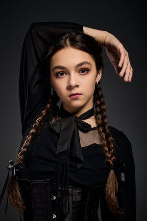 A young girl with braids poses in a gothic dress, channeling her inner Wednesday for Halloween.の写真素材