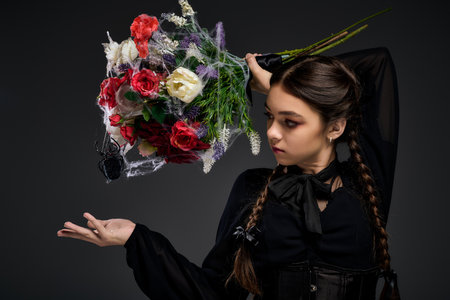 Girl with braids dressed in Wednesday style dress holds a spooky bouquet during Halloween festivities.の写真素材