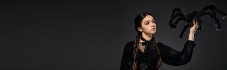 Girl in a gothic dress showcases her Halloween spirit with braids, embodying a Wednesday character, bannerの写真素材