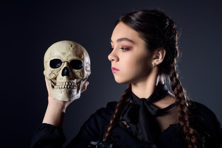 Girl with braids in a gothic costume holds a skull while embracing the Halloween spirit.の写真素材