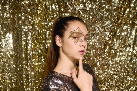 A girl with a star painted on her face poses confidently amidst golden sequins for Halloween.