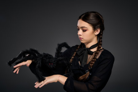 A girl dressed as a gothic character poses with a spooky spider prop during Halloween.の写真素材