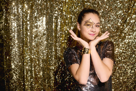 A cute girl showcases her Halloween spirit with a shining star on her face among gold sequins.