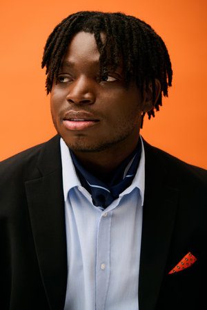 A stylish young man exudes confidence against a vibrant orange backdrop.