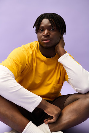 A young man exudes charm in a bright yellow shirt, relaxed against a softly colored backdrop.