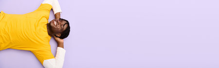 A young man in stylish clothes relaxes with a smile on a purple background.