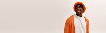 A stylish young man in a bright orange sweater and hat smiles cheerfully.のeditorial素材