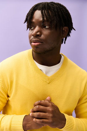 A young man wears a stylish yellow sweater, exuding confidence against a colorful backdrop.