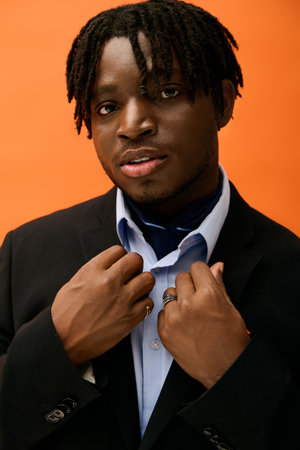 Young man exudes confidence in fashionable attire against a bright orange backdrop.