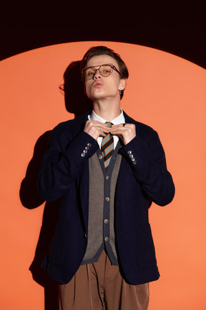 Confident teenager adjusts his tie while standing in front of a bold orange backdrop.