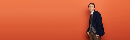 A stylish teenager leans against a bright orange wall, effortlessly embodying youth culture.の写真素材