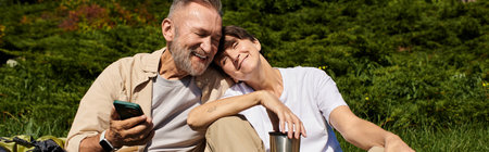 A happy senior couple takes a break while hiking in nature, sharing smiles and love, bannerの写真素材