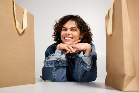 Fashionable woman with curly hair smiles joyfully while surrounded by shopping bags.の写真素材