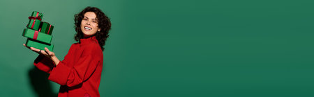 Fashionable young woman smiles brightly while showcasing wrapped gifts in vibrant colors.の写真素材