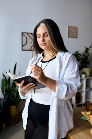 A woman with Waardenburg syndrome writes in her notebook while working remotely at home.の写真素材