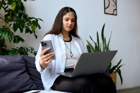A woman with Waardenburg syndrome sits on a sofa, focused on her laptop and phone while working.の写真素材