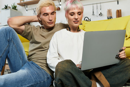A loving couple sits together on the floor, sharing laughter as they look at a laptop.の写真素材