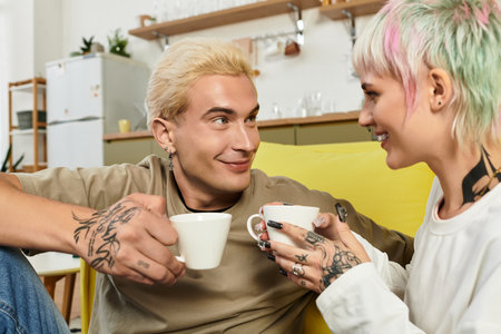 Loving couple sits on a bright couch, enjoying warm cups of coffee and sharing smiles.の写真素材