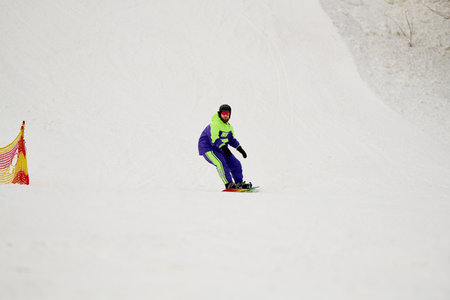 A skilled man with a beard navigates down a snowy slope while snowboarding.の写真素材