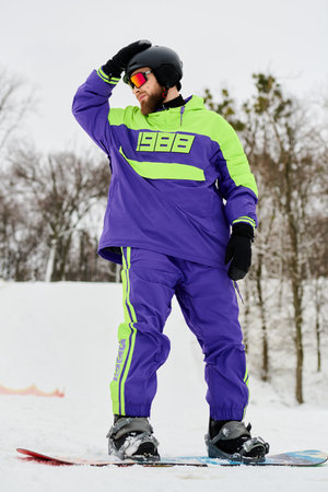A bearded man in bright winter gear snowboards down a snowy slope, enjoying the thrill.の写真素材