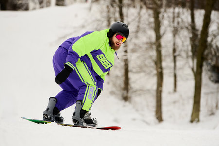 A bearded man skillfully snowboards down a snowy slope, embracing winter's thrill.の写真素材