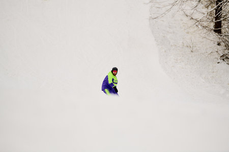 A bearded man enjoys snowboarding down a snowy slope on a clear winter day.