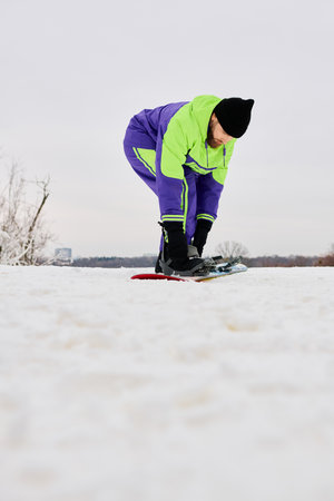 A bearded man gets ready to snowboard on a snowy slope during a winter day.の写真素材