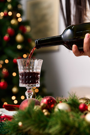 Pouring red wine into a beautiful glass while surrounded by Christmas decor and festive cheerの写真素材