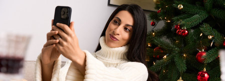 A woman enjoys taking a selfie in cozy holiday decor surrounded by Christmas cheer.の写真素材