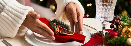 Hands carefully arranging decorative elements on a beautifully set Christmas table.の写真素材