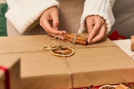 Hands wrap a holiday gift with twine, cinnamon, and dried fruit for Christmas cheer.の写真素材