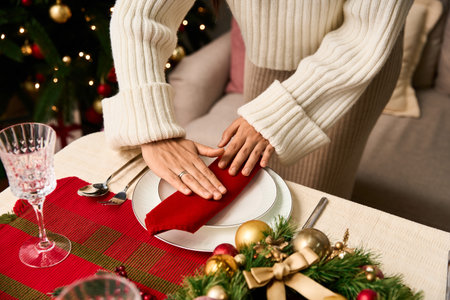 Hands neatly arrange a red napkin on a white plate, creating a warm holiday atmosphere.の写真素材