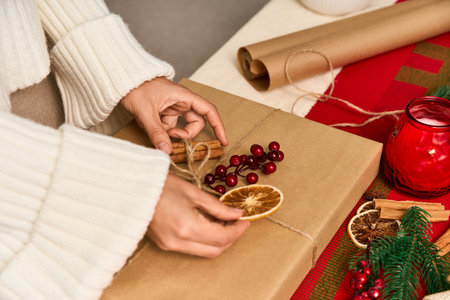 Hands place dried fruits and cinnamon on a festive Christmas gift, celebrating the season.の写真素材