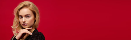 A stylish blonde in a chic black outfit poses against a bright red background for the holidays, bannerの写真素材