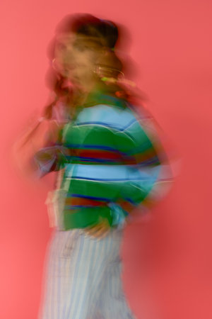 A young woman showcases her stylish outfit with confidence in front of a bright pink backdrop.の写真素材