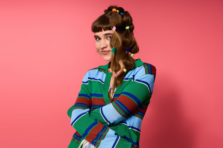 A cheerful young woman with a playful hairstyle poses confidently against a pink backdrop.