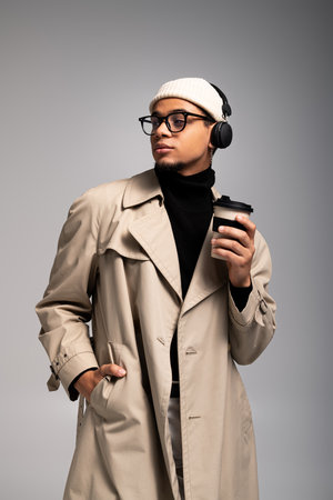 Young man exudes charm in fashionable coat, enjoying coffee while listening to music.の写真素材