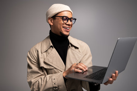 Handsome young man wears stylish attire while happily using his laptop in a chic environment.の写真素材