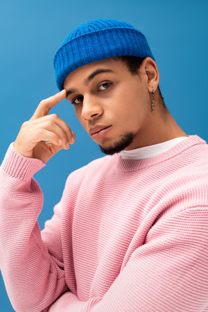 A stylish young man confidently poses in a pink sweater and blue beanie, exuding charm.の写真素材