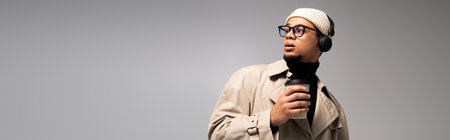 Young man dressed stylishly with headphones, looking relaxed while holding a coffee cup.の写真素材