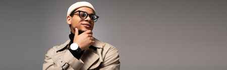 Confident young man in trendy attire poses thoughtfully against a simple background.