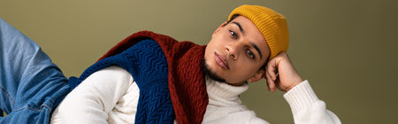 Handsome young man poses confidently in trendy attire against a softly colored backdrop.の写真素材