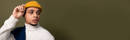 A handsome young man poses confidently in fashionable attire, wearing a bright hat and cozy sweater.の写真素材