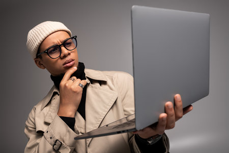 Stylish young man in trendy clothes examines his laptop in a modern setting.