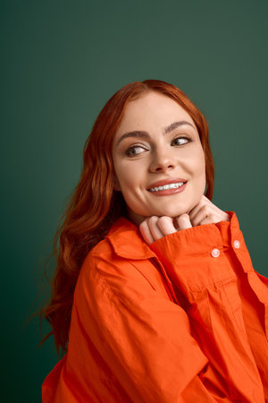 A young woman with red hair smiles in a bright orange shirt, embracing autumn fashion.の写真素材