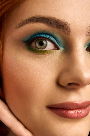 A young redhead poses with striking eye makeup, highlighting her beauty in a studio.の写真素材